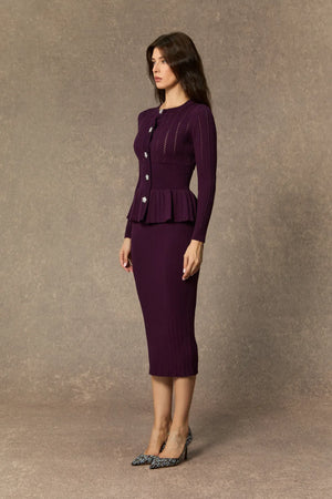 Woman wearing a purple peplum top and skirt set against a brown background