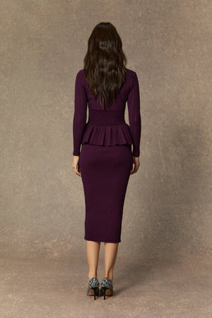 Woman wearing a purple peplum dress against a brown background
