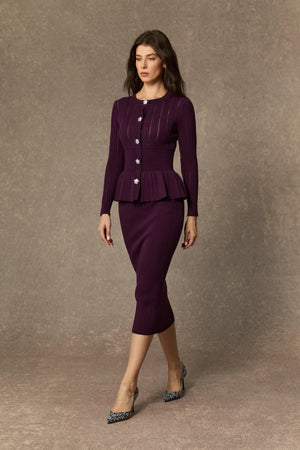 Woman wearing a purple suit with a peplum top and skirt against a brown background