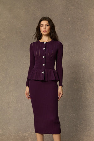 Woman wearing a purple peplum top and skirt set against a brown background