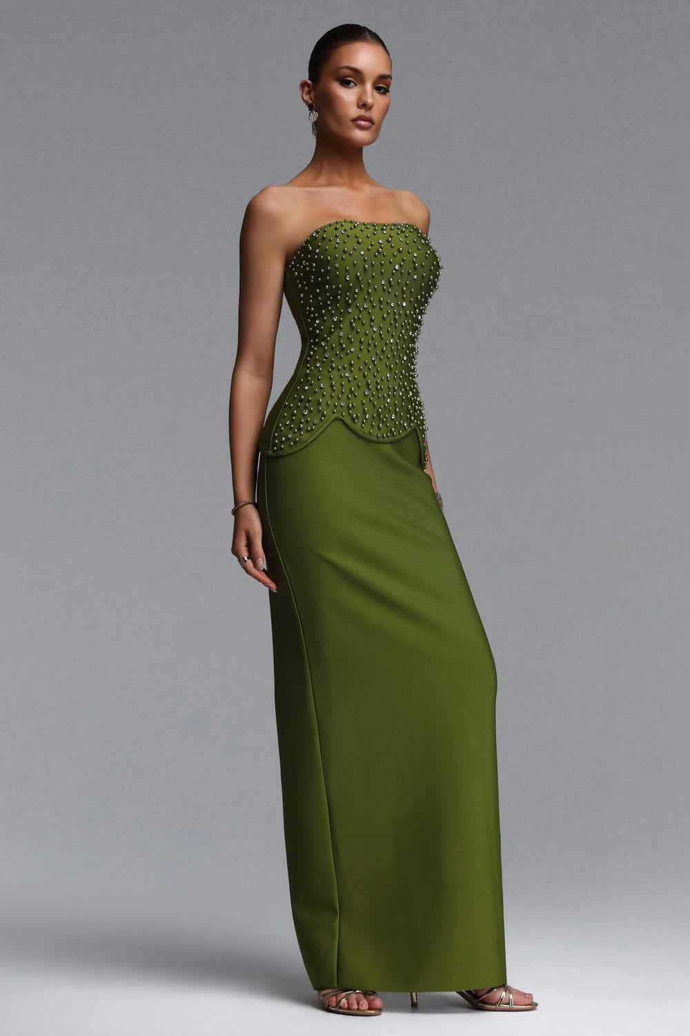 Woman wearing a green strapless gown with beaded detailing on a gray background