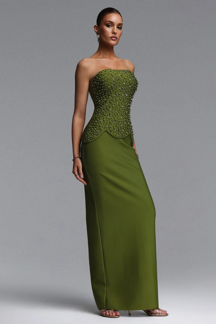 Woman wearing a green strapless gown with beaded detailing on a gray background