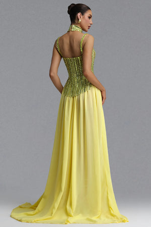 A woman modeling a floor-length yellow gown from the back, featuring a beaded corset-style back bodice and a flowing chiffon skirt, against a plain gray studio background.