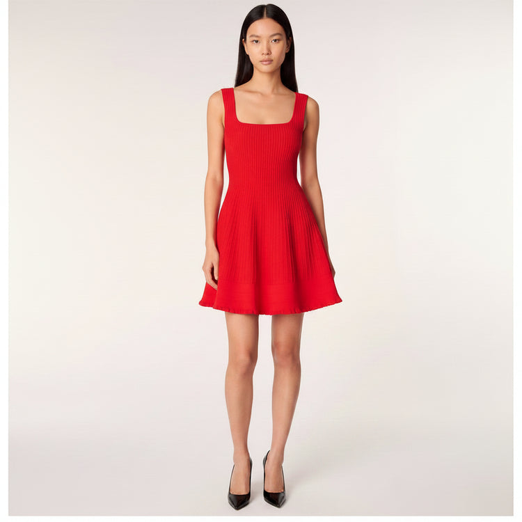 A model wearing a bright red ribbed knit sleeveless dress with a square neckline, wide shoulder straps, and a flared skirt with pockets, set against a plain light gray studio background.