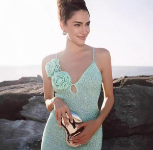 Woman in a light blue dress with floral details standing on a rocky beach.