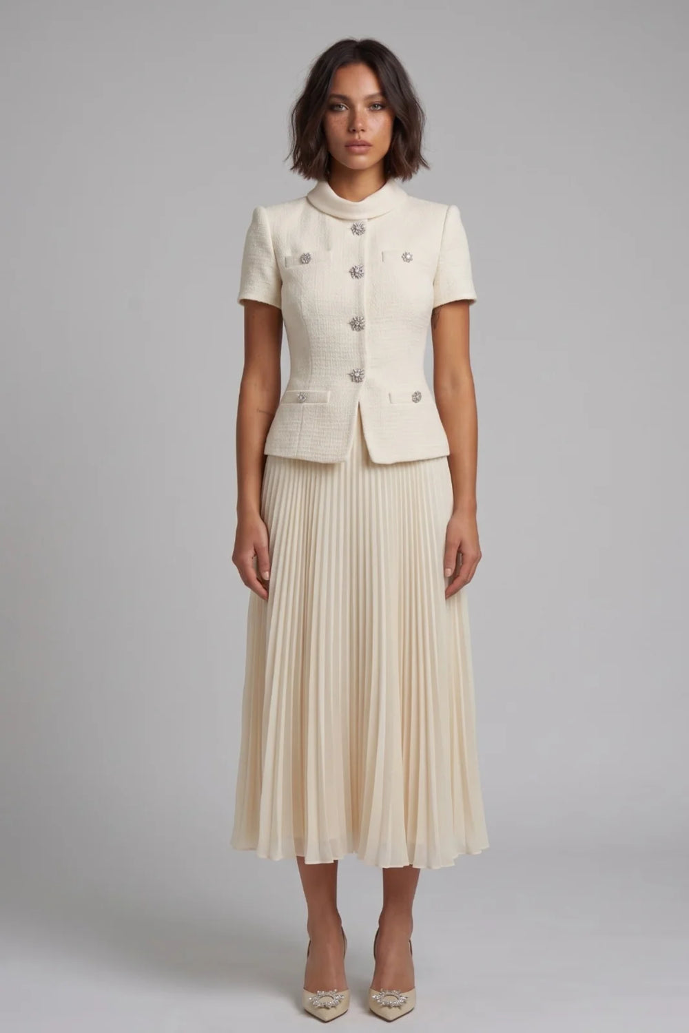 Woman wearing a cream-colored suit with a pleated skirt on a gray background