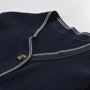 Navy blue sweater with white trim and a gold button on a light gray background
