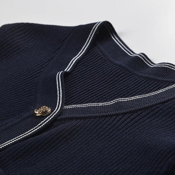 Navy blue sweater with white trim and a gold button on a light gray background