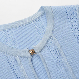 Close-up of a light blue sweater with a gold button on a white background