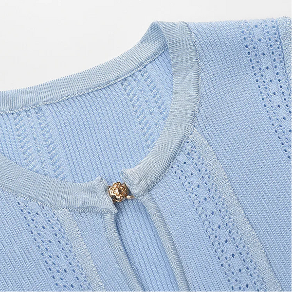 Close-up of a light blue sweater with a gold button on a white background