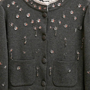Dark gray cardigan with floral embellishments on a wooden hanger against a beige background