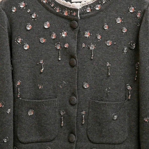Dark gray cardigan with floral embellishments on a wooden hanger against a beige background
