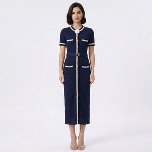 A woman modeling a navy blue short-sleeve midi dress with white and gold trim, featuring a collar with a bow, a matching belt, and decorative gold buttons on the pockets and front center.