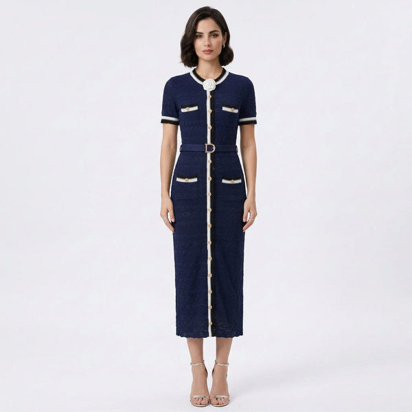 A woman modeling a navy blue short-sleeve midi dress with white and gold trim, featuring a collar with a bow, a matching belt, and decorative gold buttons on the pockets and front center.