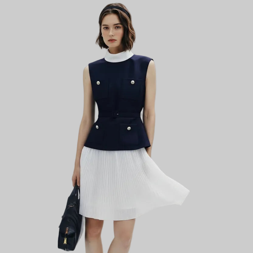 Woman wearing a navy sleeveless top with white pleated skirt on a light gray background