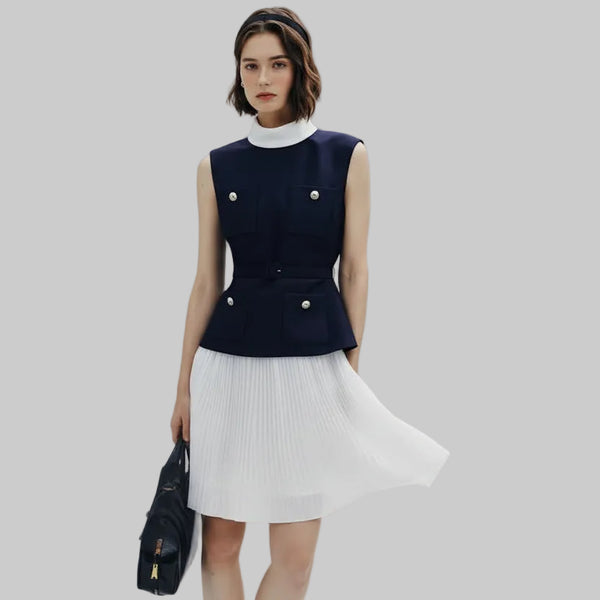 Woman wearing a navy sleeveless top with white pleated skirt on a light gray background
