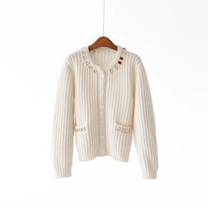 White ribbed knit cardigan with decorative buttons on a wooden hanger against a white background