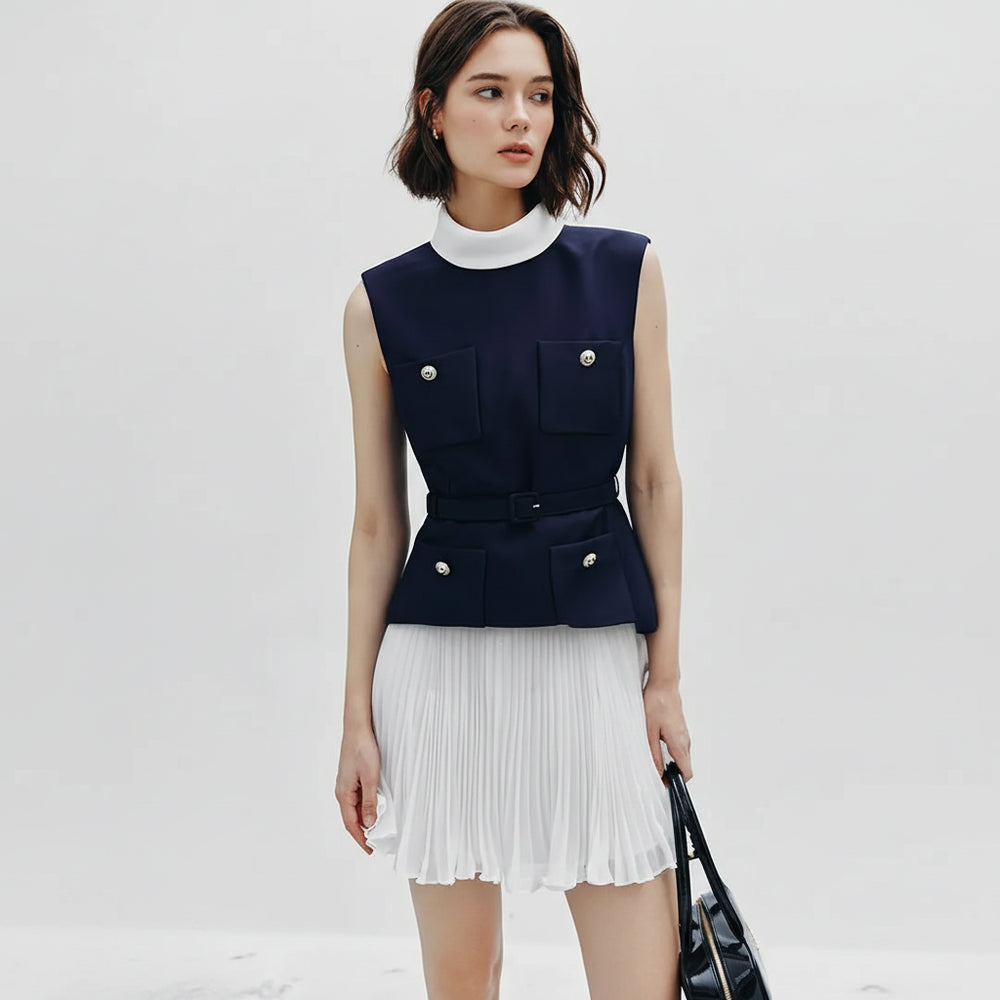 Woman wearing a navy sleeveless top with white pleated skirt on a light gray background