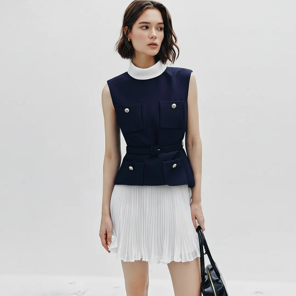 Woman wearing a navy sleeveless top with white pleated skirt on a light gray background