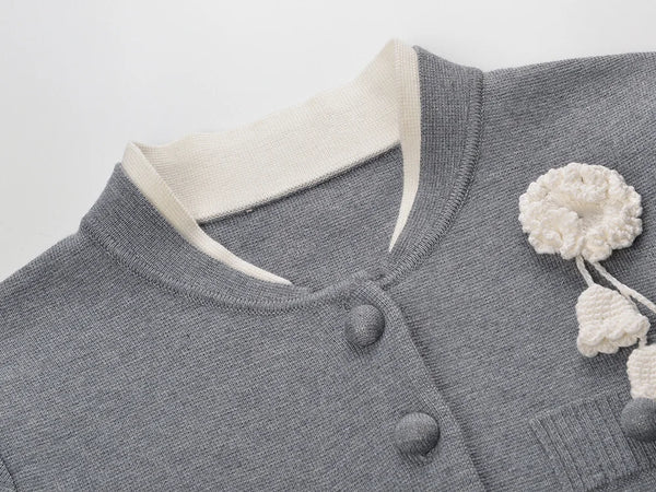 Gray sweater with white buttons and floral embellishments on a light gray background