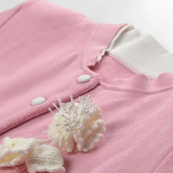 Pink baby outfit with white buttons and trim on a light background