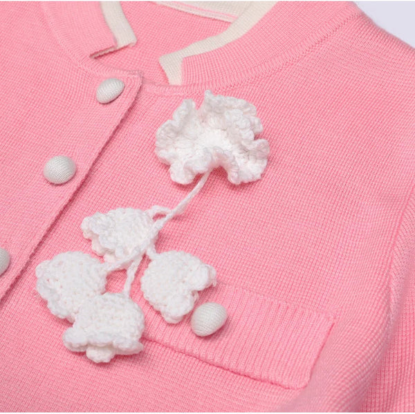 Close-up of a pink cardigan with white floral embroidery and buttons.