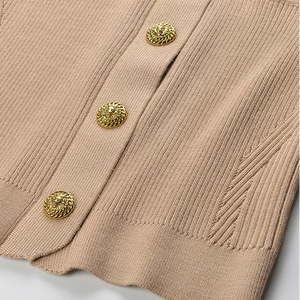 Close-up of a beige ribbed sweater with gold buttons on a light gray background