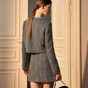 Woman in a gray patterned outfit standing against a beige wall.