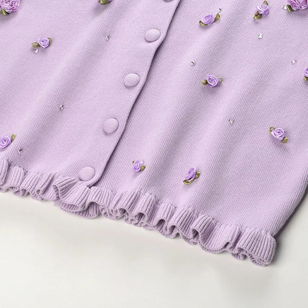Close-up of a purple cardigan with floral embellishments on a white background