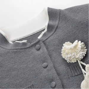 Gray cardigan with white buttons and a decorative white flower on a light gray background