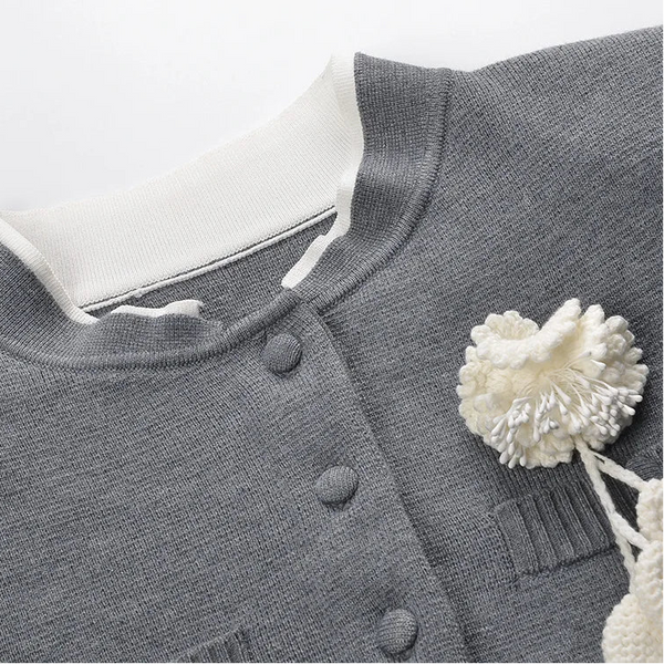 Gray cardigan with white buttons and a decorative white flower on a light gray background