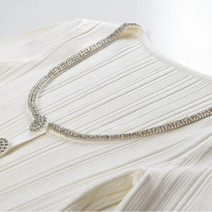 Close-up of a white dress with a decorative silver trim on a light background