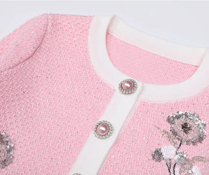 Pink textured garment with floral embellishments and buttons on a light gray background