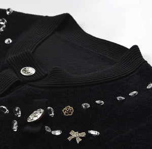 Black sweater with decorative buttons and embellishments on a white background