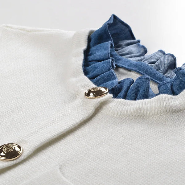 Close-up of a white sweater with blue ruffled collar and gold buttons on a light background