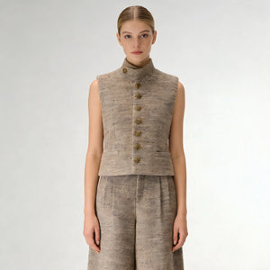 Woman wearing a beige sleeveless jacket with gold buttons on a white background
