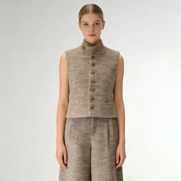 Woman wearing a beige sleeveless jacket with gold buttons on a white background