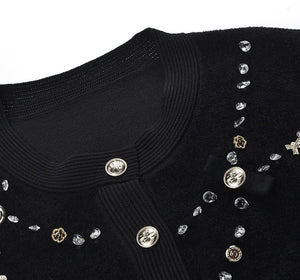 Black sweater with decorative buttons and embellishments on a white background