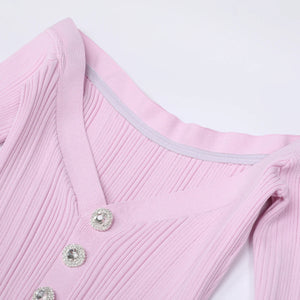 Close-up of a pink ribbed sweater with decorative buttons on a light gray background