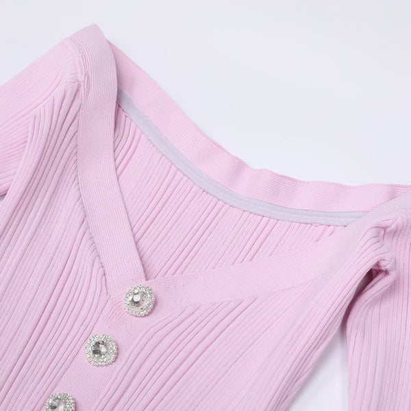 Close-up of a pink ribbed sweater with decorative buttons on a light gray background