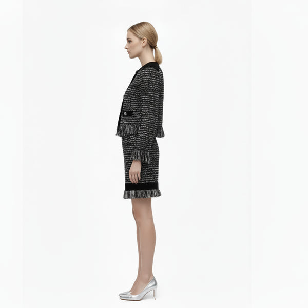 Woman wearing a black and white tweed dress with a matching handbag on a white background