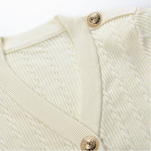 Close-up of a cream-colored sweater with gold buttons on a white background