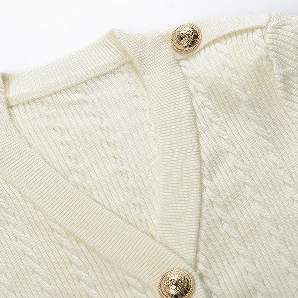 Close-up of a cream-colored sweater with gold buttons on a white background