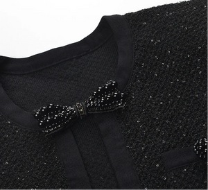 Black sequined garment with a bow detail on a white background
