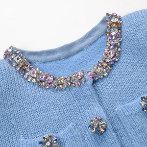Close-up of a blue sweater with decorative gemstones on a white background
