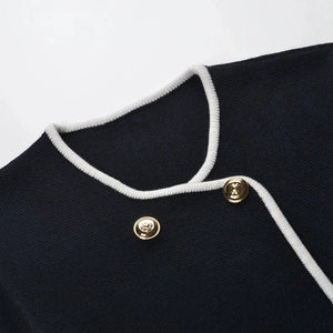 Close-up of a black garment with white trim and gold buttons on a white background