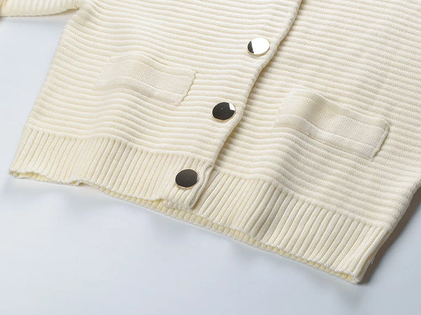 Close-up of a cream-colored ribbed cardigan with buttons on a light gray background