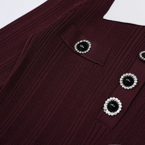 Close-up of a burgundy ribbed sweater with black button centers and pearl-like trim.