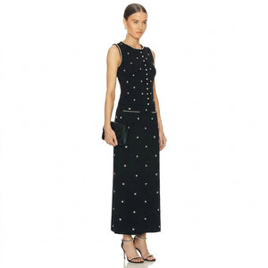 A woman modeling a sleeveless black maxi dress with white embroidered star patterns, white piping details, and a white button-up front, set against a plain white background.