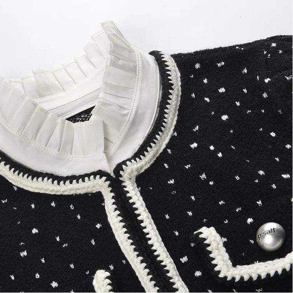 Black sweater with white polka dots and ruffled collar on a white background
